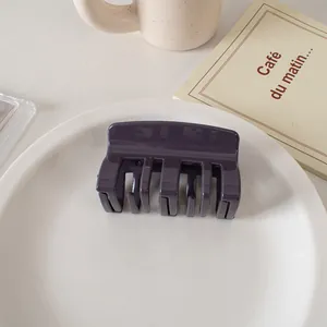 Close-up of a glossy deep purple hair claw clip on a white decorative ceramic tray