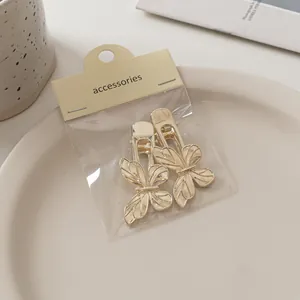 Detailansicht von zwei goldenen Schmetterlings-Haarspangen auf Keramikteller mit Verpackung
