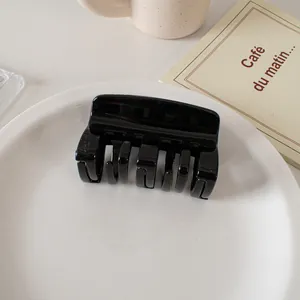 Glossy black medium square hair claw clip on a ceramic plate with French cafe card