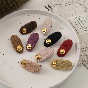 Set of eight colorful plush wool hair clips with gold metal buttons in a ceramic tray