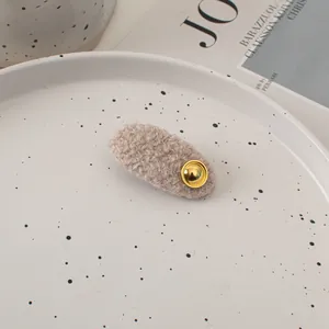 Close-up of beige fuzzy wool hair clip with a round gold emblem on a ceramic plate