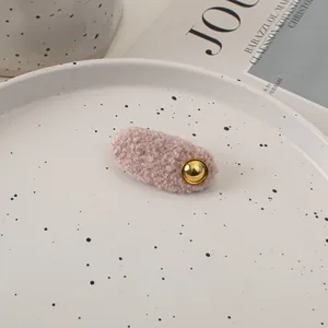 Detailed shot of a mauve plush wool hair clip with a vintage round golden button