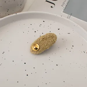 Detail of khaki plush teddy fleece hair clip with a gold metal button in a ceramic tray