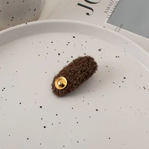 Detail of a brown fuzzy plush hair clip with a gold metal button in a ceramic dish
