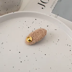 Detail of a beige teddy fleece hair clip with a gold metal button on a ceramic tray