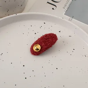 Close-up of a dark red plush wool hair clip with a gold metallic button in a ceramic tray
