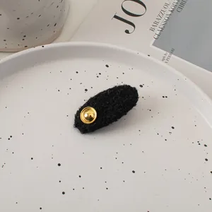 Close-up of black textured tweed oval hair clip with gold metal rivet on a stylish tray