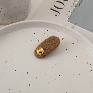 Close-up of brown plush wool hair clip with a vintage gold button on a ceramic plate