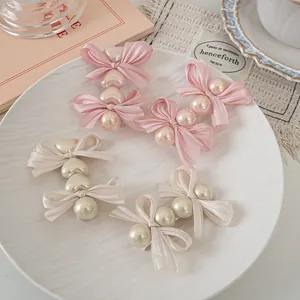Detailed view of pink and cream satin bow hair clips with pearls on a ceramic tray