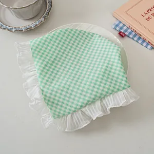 Detailaufnahme des grün karierten Haartuchs mit gerüschten Spitzenkanten auf dem Tisch