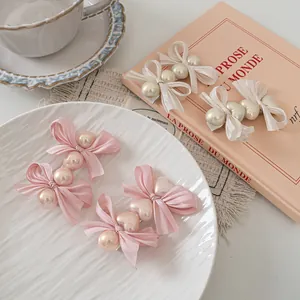Detail of pink and cream satin bow hair clips with pearls on an elegant white plate