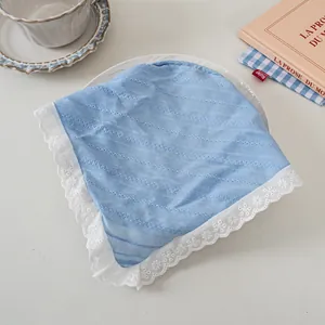 Detail eines hellblauen Baumwolltuches mit weißer Spitze auf einem gedeckten Tisch