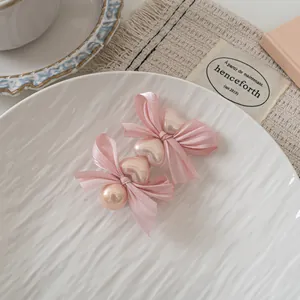 Detail of pink satin bow hair clips with heart-shaped pearls on a decorative white plate