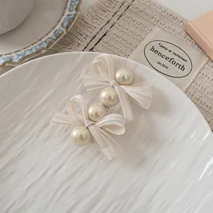 Detail of cream bow hair clip with faux pearls on white ceramic plate, French style