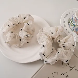 Detail of off-white lace mesh scrunchies with black bow patterns on a ceramic plate