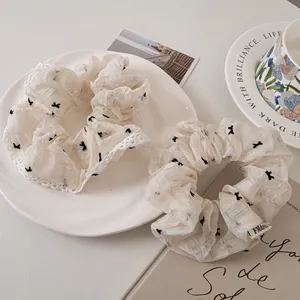Close-up of white mesh scrunchies with black bow prints and delicate lace edging