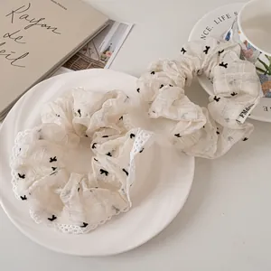 Set of two cream lace mesh scrunchies with black bow patterns and brand tag on a tray