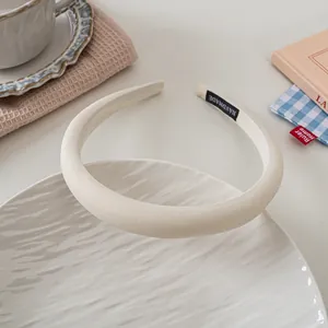 Detail of cream handmade sponge headband with textured fabric and woven label on a ceramic tray