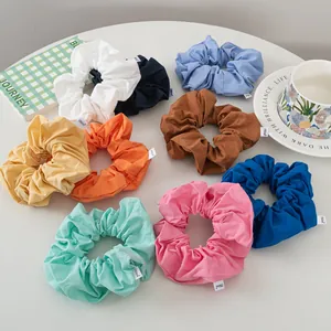 Flat lay of colorful pleated fabric hair scrunchies in pastel tones with logo tags