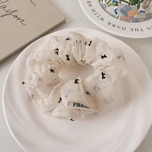 Detail of a creamy white lace scrunchie with embroidery on a ceramic plate