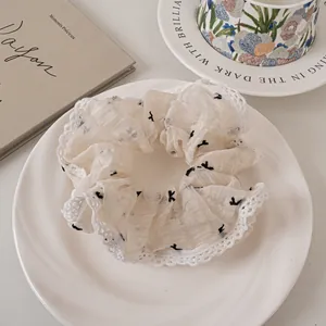 Close-up of beige lace scrunchie with delicate mesh and black butterfly pattern detail
