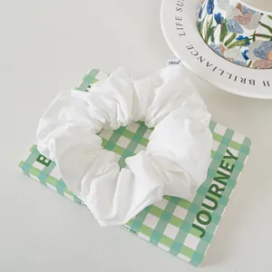 Close-up of white textured fabric scrunchie with FMdrea brand woven label on checkered box