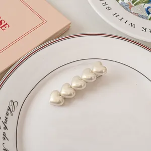 Dettaglio di un elegante fermaglio per capelli con cuori perlati su un piatto bianco