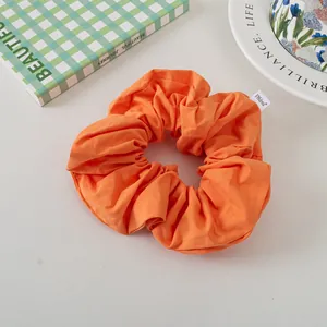 Detail of orange fabric scrunchie with white brand label on a minimalist aesthetic background