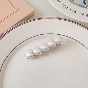 Dettaglio di cinque perle bianche a forma di cuore su un fermaglio in metallo argentato