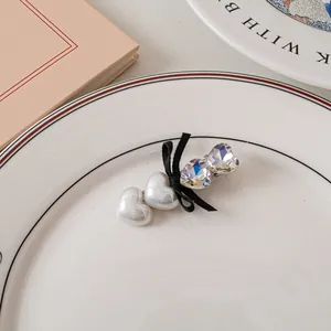 Dettaglio di fermaglio a cuore con perle bianche e fiocco in cristallo su piatto bianco