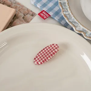 Close-up of a vintage red houndstooth oval hair clip on a decorative ceramic tray