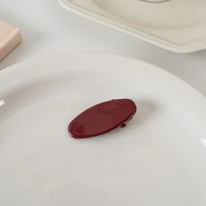 Vue détaillée d'une barrette ovale rouge foncé dans un plateau blanc en céramique lisse