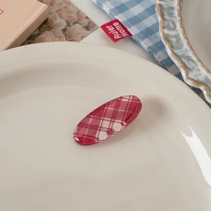 Detailed view of red plaid oval hair clip on a white plate with aesthetic background