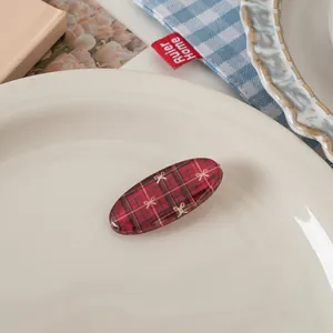 Detailed view of red plaid oval hair clip with bow pattern on a white ceramic plate