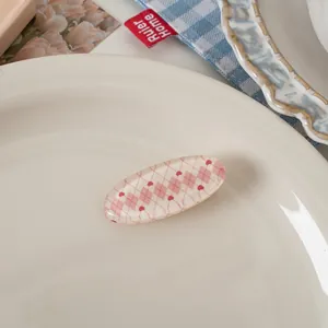 Close-up of oval resin hair clip featuring pink argyle pattern and red mini hearts