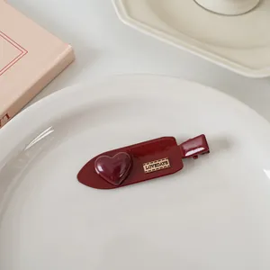 Détail de la pince à cheveux cœur bordeaux avec gravure dorée LOVEDAYS sur plateau