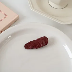 Détail d'une pince à cheveux ondulée bordeaux avec texture brillante sur plat