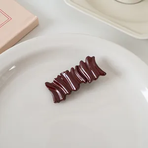 Détail d'une pince à cheveux rouge bordeaux brillante avec texture ondulée sur plat blanc