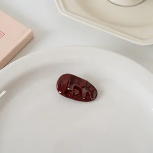 Détail de la pince à cheveux ondulée rouge bordeaux brillant sur plateau céramique