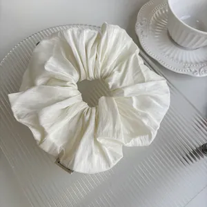 Detailed view of white pleated satin scrunchie on decorative glass tray for hair styling