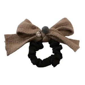 Chouchou nœud en tricot marron avec pompon gris et pendentif smiley sur fond blanc