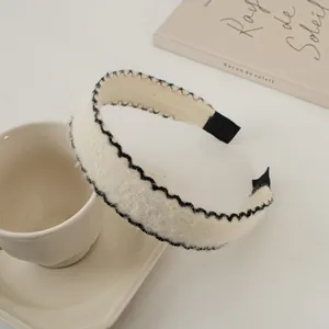 Détail du serre-tête en peluche crème avec broderie festonnée noire sur une tasse blanche