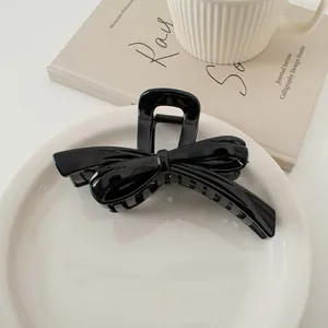 Glänzende schwarze Schleifen-Haarklammer auf weißem Keramikteller für elegantes Haarstyling
