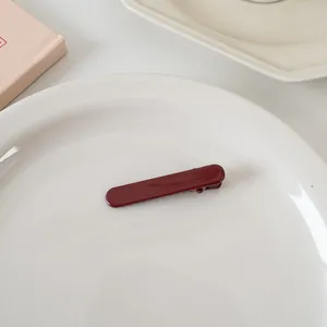 Vue détaillée d'une pince à cheveux rectangulaire rouge foncé sur une assiette