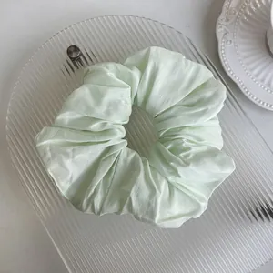 Detailed close-up of light mint green satin scrunchie with soft pleated texture and silk-like shine
