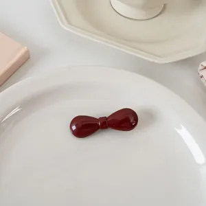 Détail d'une pince à cheveux nœud rouge foncé brillant sur un plateau en céramique épuré