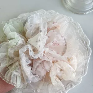 Blumen-Schleifen-Organza-Haargummis in Pastellfarben auf einem weißen Dekoteller