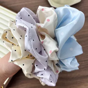 Close-up of four large satin polka dot scrunchies in cream, purple, white, and blue