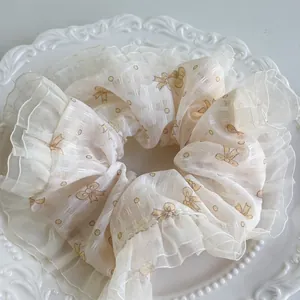 Detail eines cremefarbenen Spitzen-Scrunchies mit gelben Schleifen auf Netzgewebe