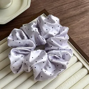 Detail of lavender satin scrunchie with black polka dots and a small side label